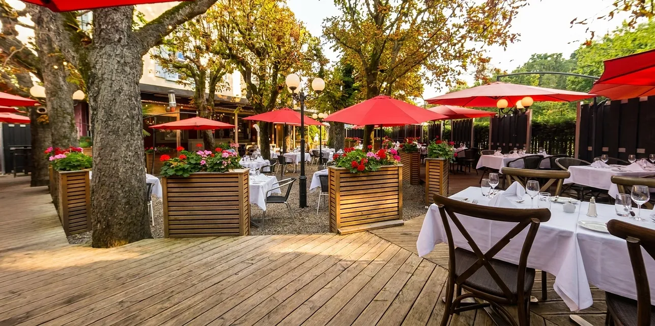 Gartenterrasse mit roten Sonnenschirmen unter alten Bäumen.